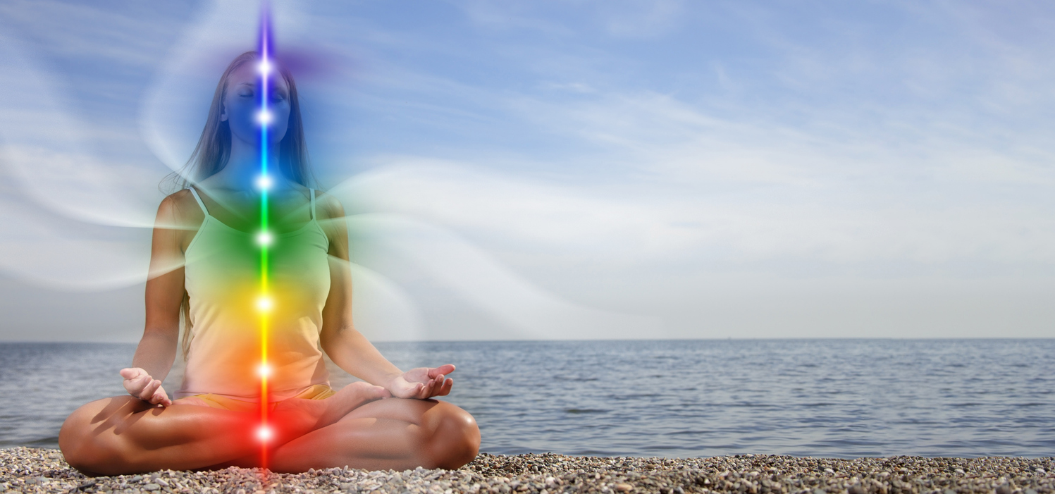 Lady meditating on beach with her kundalini awakened and chakras lit up.